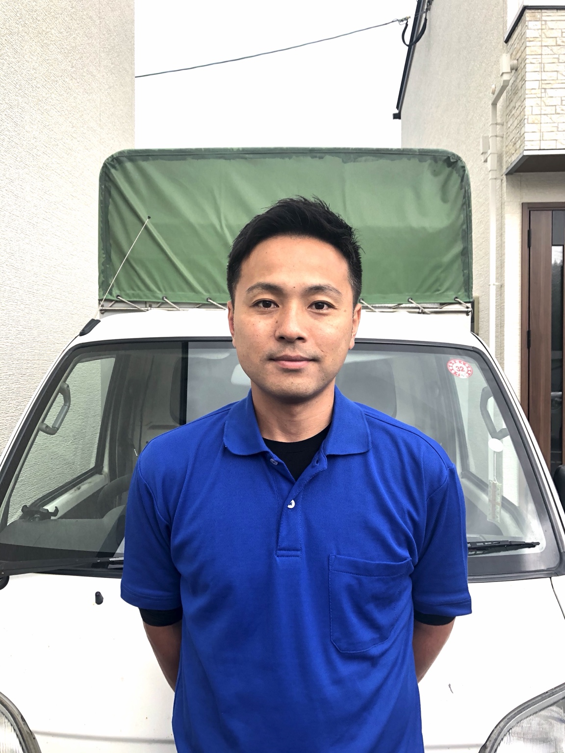 青い作業着で軽トラックの前に立つ店長の園田直樹